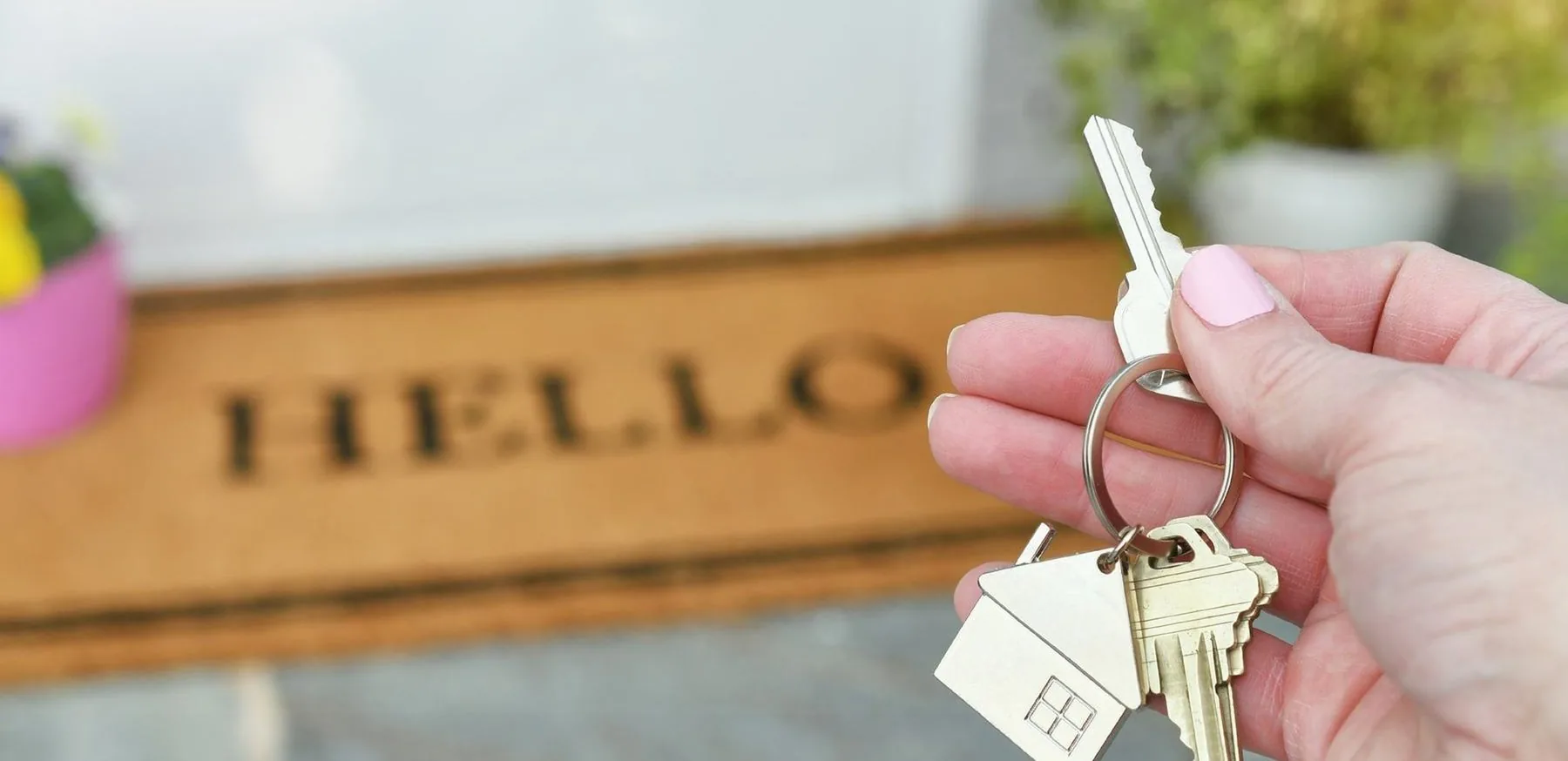 Keys to a new home held over a HELLO doormat